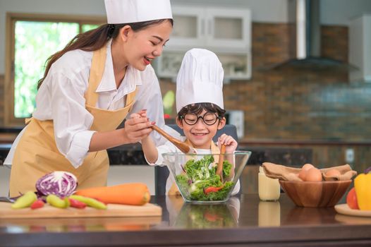 Happy beautiful Asian woman and cute little boy with eyeglasses prepare to cooking in kitchen at home. People lifestyles and Family. Homemade food and ingredients concept. Two Thai people life