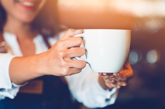 Closeup of professional female barista hand making and holding white cup of coffee. Happy young woman at counter bar in restaurant background. People lifestyles and Business occupation concept