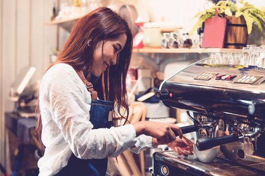 Professional female barista hand making cup of coffee with coffee maker machine in restaurant pub or coffee shop. People and lifestyles. Business food and drink concept.  Happy shop owner entrepreneur