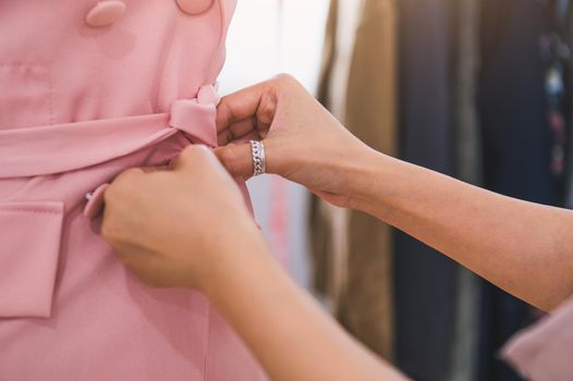 Closeup of female fashion designer girl hand making fit on formal dress uniform clothes on mannequin model. Fashion designer stylish showroom. Sewing and tailor concept. Creative dressmaker stylist