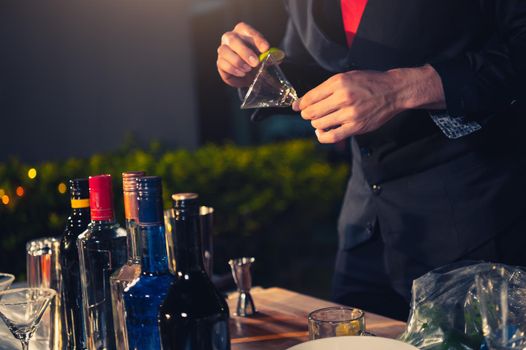Professional bartender preparing fresh lime lemonade cocktail in drinking wine glass with ice at night bar clubbing counter. Occupation and people lifestyles concept. Outdoor background