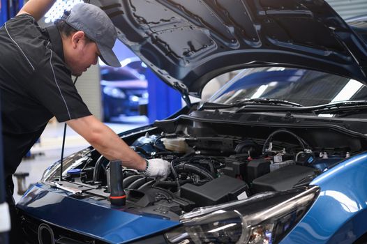 Asian male auto mechanic examine car engine breakdown problem in front of automotive vehicle car hood. Safety technical inspection care check service maintenance for customer before long road trip