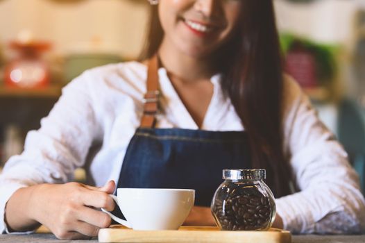 Closeup of white coffee cup with beautiful Asian woman barista background for serving to customer. Job and occupation. Food and drink beverage. Coffee shop and Cafe. Business and restaurant ownership