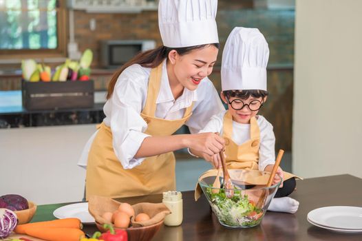 Happy beautiful Asian woman and cute little boy with eyeglasses prepare to cooking in kitchen at home. People lifestyles and Family. Homemade food and ingredients concept. Two Thai people life