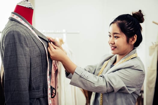 Asian female fashion designer girl making fit on the formal suit uniform clothes on mannequin model. Fashion designer stylish showroom. Sewing and tailor concept. Creative dressmaker stylist.