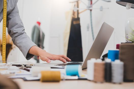 Closeup of female fashion designer hand working in clothing shop studio and using laptop computer to contact customer. Woman creating design new collection . Tailor sewing. People lifestyle concept