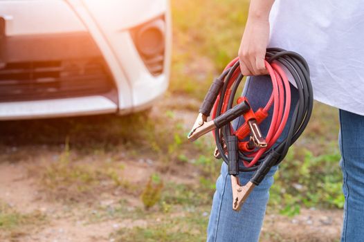 Closeup of woman hand holding battery cable copper wire for repairing broken car by connect battery with red and black line to electric terminal by herself. Car maintenance and transportation concept