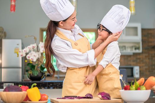 Happy cute little boy with eyeglasses looking beautiful Asian woman mother each other while prepare to cooking in kitchen at home. People lifestyles and Family. Homemade food and ingredients concept.