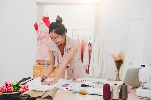 Attractive Asian female fashion designer working in home office workshop. Stylish fashionista woman creating new cloth design collection. Tailor and sewing. People lifestyle and occupation concept