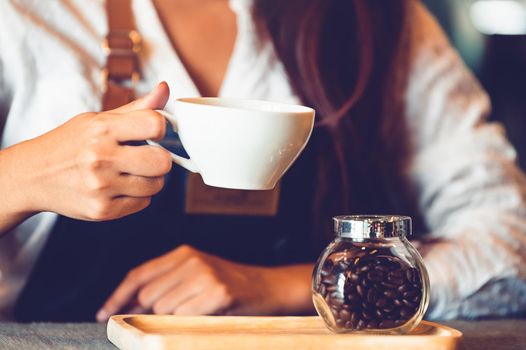 Closeup of professional female barista hand making and holding white cup of coffee. Happy young woman at counter bar in restaurant background. People lifestyles and Business occupation concept
