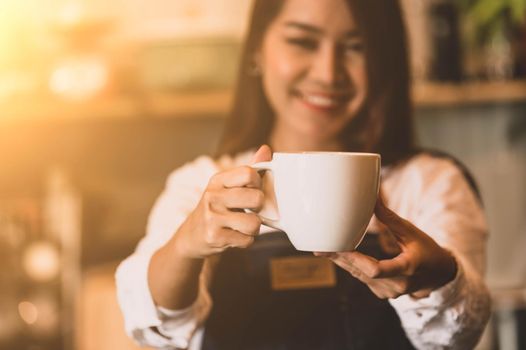 Closeup of white coffee cup with beautiful Asian woman barista background for serving to customer. Job and occupation. Food and drink beverage. Coffee shop and Cafe. Business and restaurant ownership