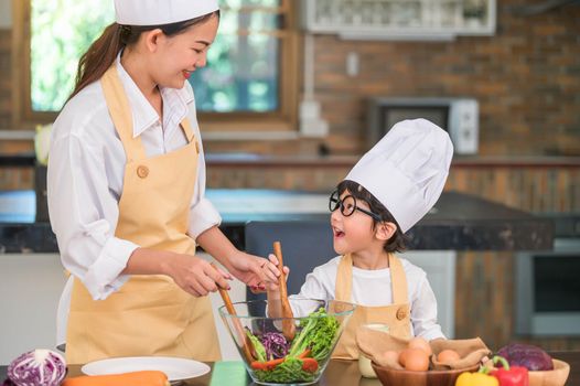 Happy beautiful Asian woman and cute little boy with eyeglasses prepare to cooking in kitchen at home. People lifestyles and Family. Homemade food and ingredients concept. Two Thai people life