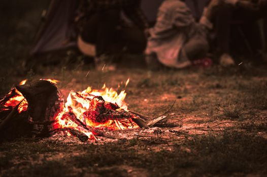 Sparking bonfire with tourist people sit around bright bonfire near camping tent in forest in summer night background. Group of student at outdoor fire fuel. Travel  activity and long vacation weekend