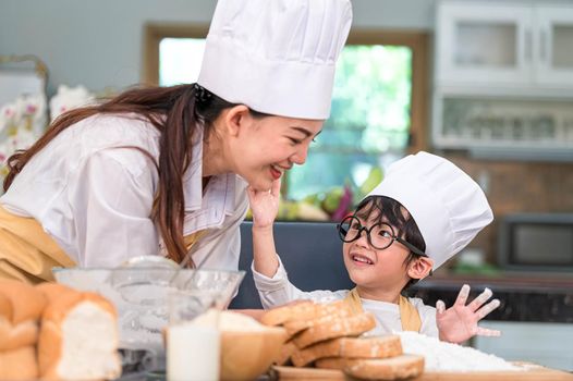 Cute little Asian boy painting beautiful woman face with dough flour. Chef team playing and baking bakery in home kitchen funny. Homemade food and bread. Education teamwork and learning concept.