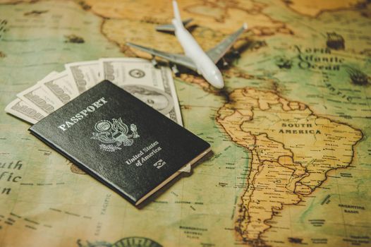 Top view of tourist planning props and travel accessories with American passport, airplane and US dollar banknote money on old grunge style map. Holiday and vacation. Tourism long weekend concept.