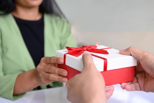 Closeup of hands giving gift box in Christmas day and new year festival to each other with woman background. Holiday and event. Surprising giftbox in dating on end year party. People lifestyle concept