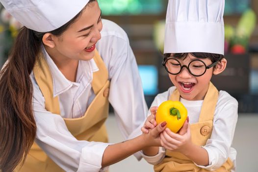 Portrait cute little Asian happy boy chef interested in cooking with mother funny in home kitchen. People lifestyles and Family. Homemade food and ingredient concept. Baking Christmas cake and cookies