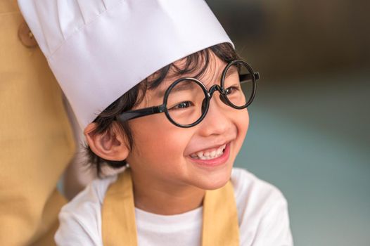 Portrait cute little Asian happy boy interested in cooking with mother funny in home kitchen. People lifestyles and Family. Homemade food and ingredients concept. Baking Christmas cake and cookies