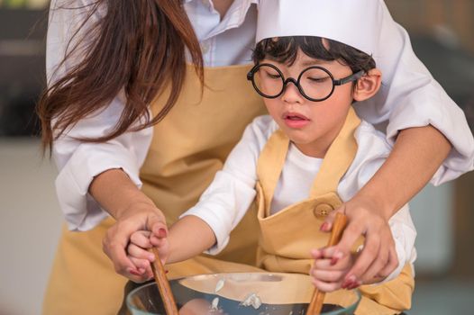 Happy cute little boy with eyeglasses and beautiful Asian mother prepare to cooking in kitchen at home. People lifestyles and Family. Homemade food and ingredients concept. Two Thai people life