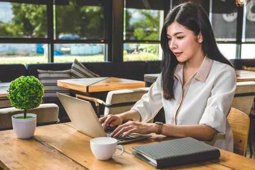 Asian woman working with laptop in coffee shop. People and Lifestyles concept. Job and occupation working and freelance theme.