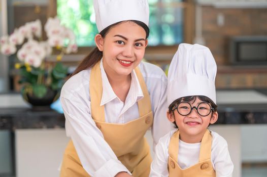 Portrait of beautiful Asian woman and cute little boy with eyeglasses prepare to cooking in kitchen at home. People lifestyles and Family. Homemade food and ingredients. Two Thai people looking camera