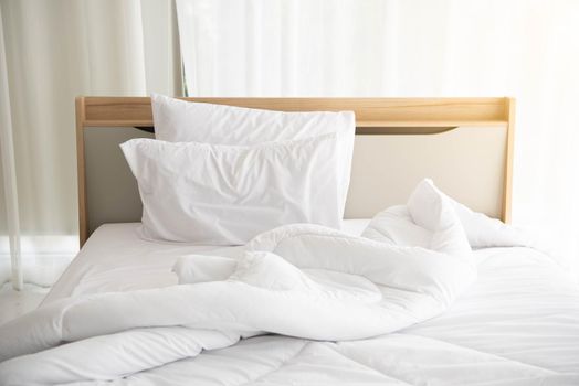 White unmade bed in the morning with sunshine with white curtain background in elegant home. Interior design and luxury furniture concept. Indoors lifestyle and Lazy activity theme.