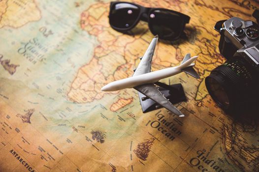Tourist planning props and travel accessories with airplane, digital camera and sunglasses on old grunge style map desktop. Holiday destination and vacation concept. Copyspace