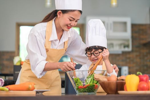 Happy beautiful Asian woman and cute little boy with eyeglasses prepare to cooking in kitchen at home. People lifestyles and Family. Homemade food and ingredients concept. Two Thai people life