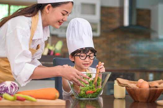 Happy beautiful Asian woman and cute little boy with eyeglasses prepare to cooking in kitchen at home. People lifestyles and Family. Homemade food and ingredients concept. Two Thai people life