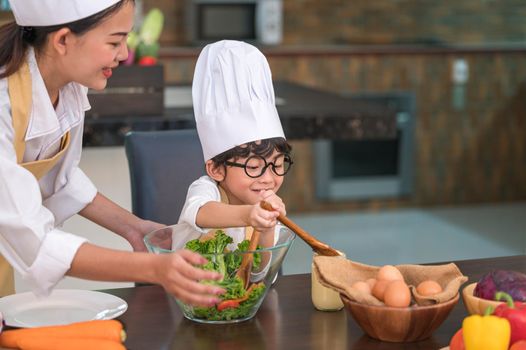 Happy beautiful Asian woman and cute little boy with eyeglasses prepare to cooking in kitchen at home. People lifestyles and Family. Homemade food and ingredients concept. Two Thai people life