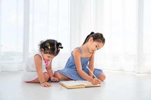 Happy two sister drawing in sketch book together at home or nursery. People lifestyle and kids play. Education and Children concept. Diverse ethnicity and ages. Back to school theme.
