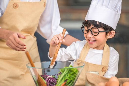 Cute little Asian happy boy interested in cooking with mother funny in home kitchen. People lifestyles and Family. Homemade food and ingredients concept. Two Thai people making ketogenic diet salad