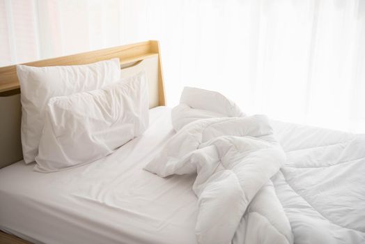 White unmade bed in the morning with sunshine with white curtain background in elegant home. Interior design and luxury furniture concept. Indoors lifestyle and Lazy activity theme.