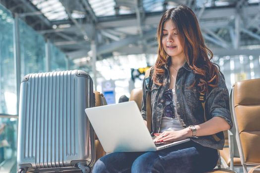 Beauty Asian woman using laptop with suitcase while waiting for take off flight. Woman sitting in airport terminal. People and lifestyle concept. Technology and travel theme. Portrait theme