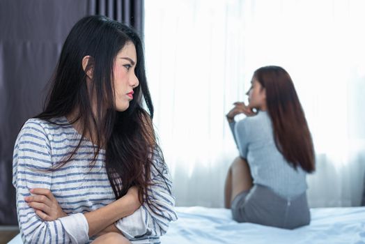 Asian woman having stressed after conflict with girlfriend in bedroom. Serious and negative thinking people. Upset and unhappy female concept. Lifestyle and family issues. LGBT theme