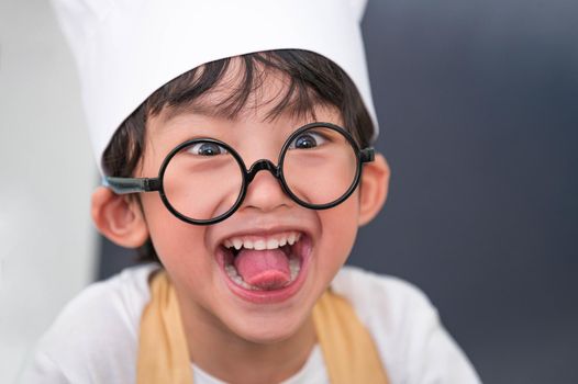 Portrait cute little Asian happy boy doing funny tongue face and interested in cooking in home kitchen. People lifestyles and Family. Homemade food ingredients concept. Baking Christmas cake and cook