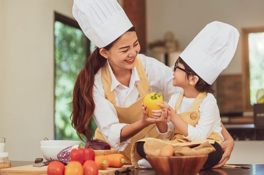 Happy Asian family in kitchen. Mother and son in chef hat preparing food in home kitchen together. People lifestyle and Family. Homemade food and ingredients concept. Two Thai people in teaching class