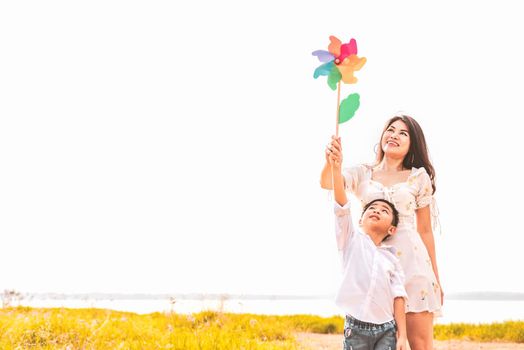 Little Asian boy and his mom playing colorful rainbow turbine in meadow. Mother and son playing together. Celebrating in Mother day and appreciating concept. Summer people and lifestyle theme.