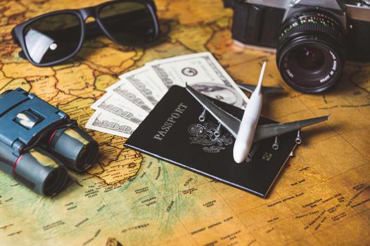 Tourist planning props and travel accessories with American passport, airplane, digital camera, telescope, sunglasses and US dollar banknote money on old grunge style map. Holiday and vacation concept.