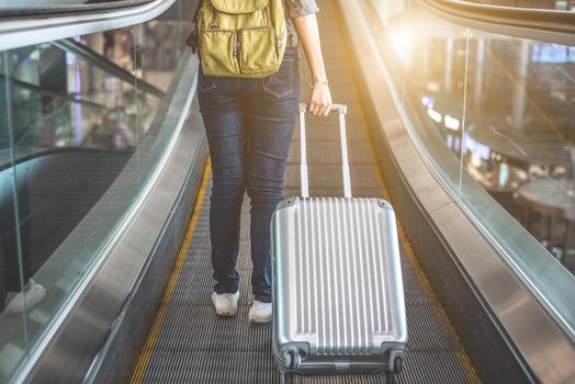 Back view of beauty woman traveling and holding suitcase on escalator in airport. People and Lifestyles concept. Travel around the world theme. Adventure and business trip theme.