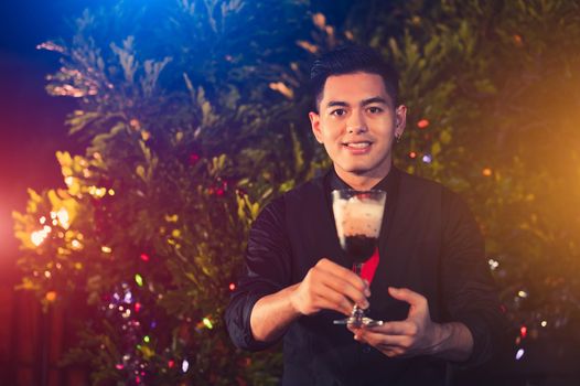 Young Asian male bartender mixing alcohol drink cocktail in glass wine at outdoors night club. People lifestyles and occupation. Job and occupation concept. Christmas and New year event festival theme