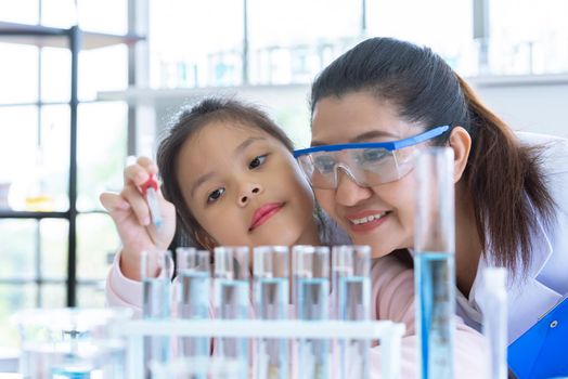Scientist girl and teacher dropping solution substance liquid with pipette into test tube in lab classroom together. Education and Science. Micro and Nano technology. E-Healthcare and medical concept.