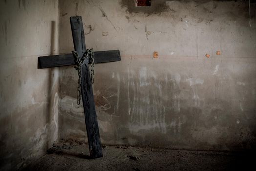 Black crucifix against wall with hanging steel chain and gun. Halloween day party festival celebration. Ancient sign of religion concept. Dark and scary tone