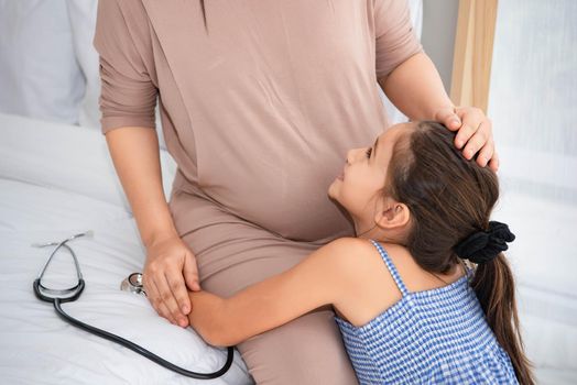 Cute daughter hugging mother and listening to voice of baby in mother belly for checking and looking at mom face. Pregnant and parents. Health and medical. People lifestyles and family love concept.