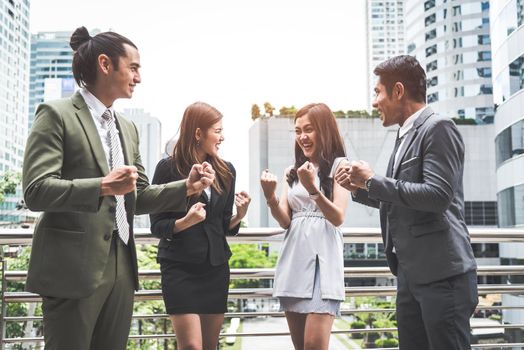 Portrait of successful group of business people at outdoor urban. Happy businessmen and businesswomen raising hand as team in satisfaction gesture. Successful group of people smiling after achievement