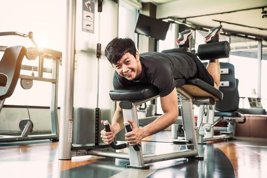 Asian sport man stretching and lifting weight by two legs when facing down for stretching muscle at fitness gym at condominium background. Sport and People lifestyles concept.