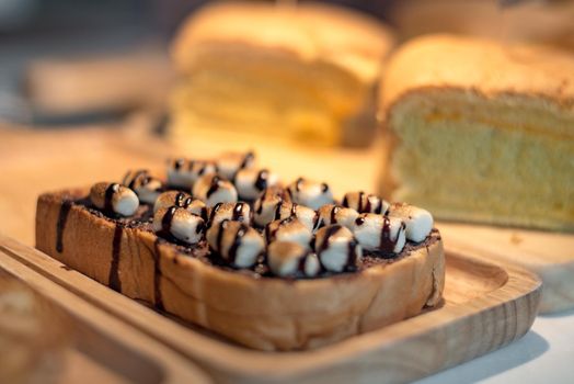 Sliced toasted bread with marshmello topping with chocolate sauce on wooden plate. Food and drinks concept. Bakery and coffee shop theme.