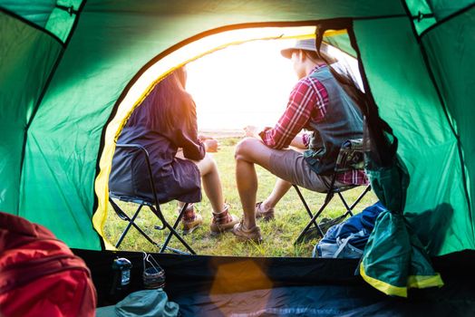 Male and female campers talking each others in front of camping tent. People and lifestyles concept. Picnic and travel concept. Nature in summer theme. Back view and inside of tent angle