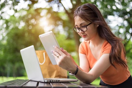 Beauty Asian woman using tablet in the park. Technology and lifestyles concept. Outdoor and nature theme.