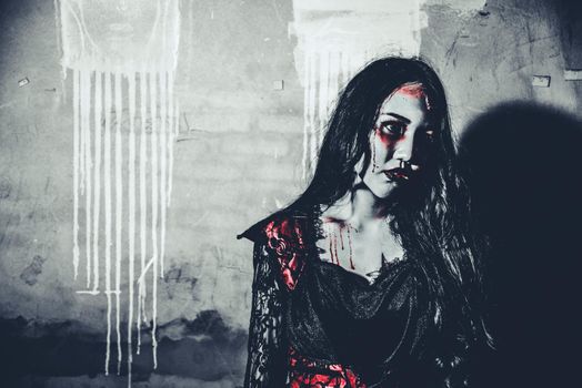 Female zombie corpse standing in front of grunge wall in abandoned house. Horror and Ghost concept. Halloween day festival and scary movie theme. Haunted house theme. Dark tone film